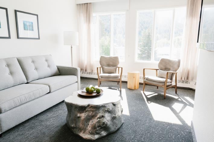 A lounge of chairs and sofa sit below a bright window letting in sunlight.